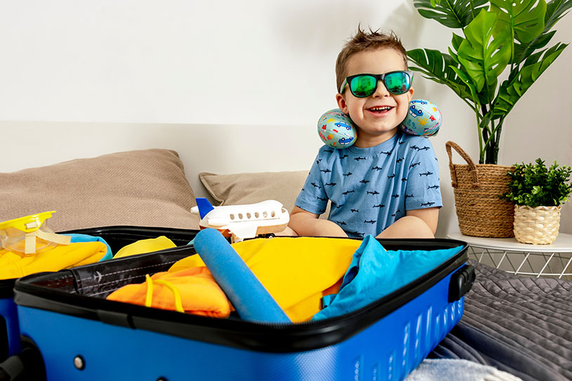 a boy sitting on a bed with a suitcase full of clothes